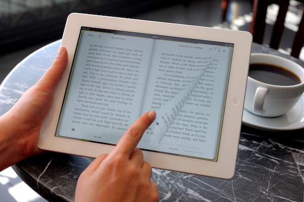 Reading E-book with iPad 3 close up of a person holding a light bulb that is glowing and writing in a notebook.