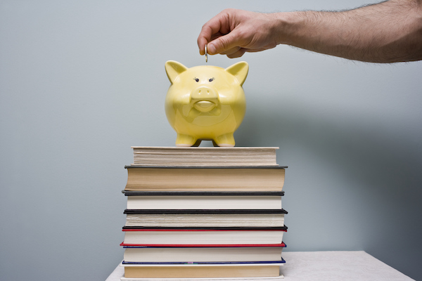 Man puts coin in piggy bank Saving Money for School close up of a person holding a light bulb that is glowing and writing in a notebook.