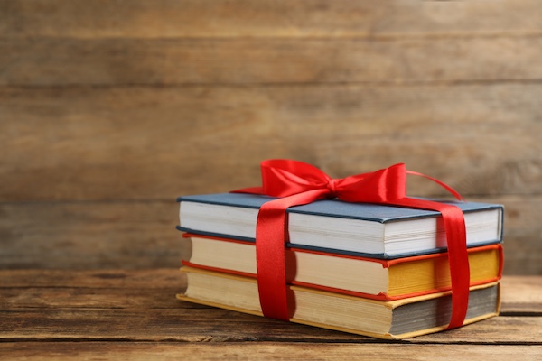 Different books tied with red ribbon on wooden table, space for text close up of a person holding a light bulb that is glowing and writing in a notebook.