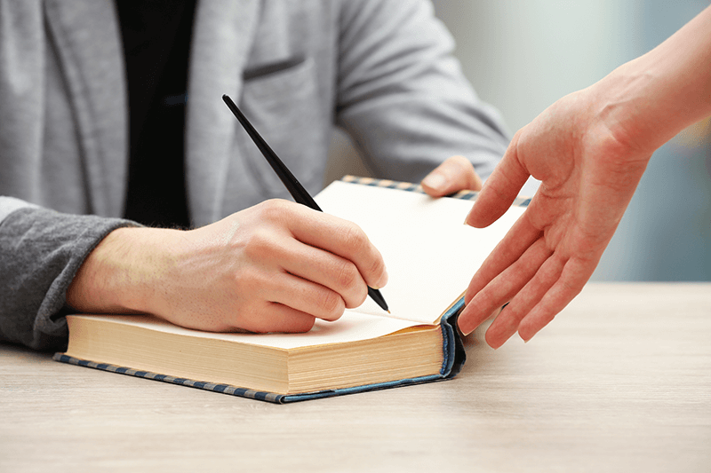 Author signing autograph in own book at wooden table