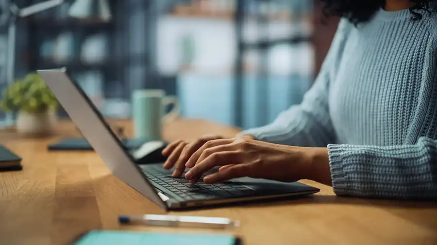 Close up on hands of a female working on laptop computer at cozy home living room while sitting at a table