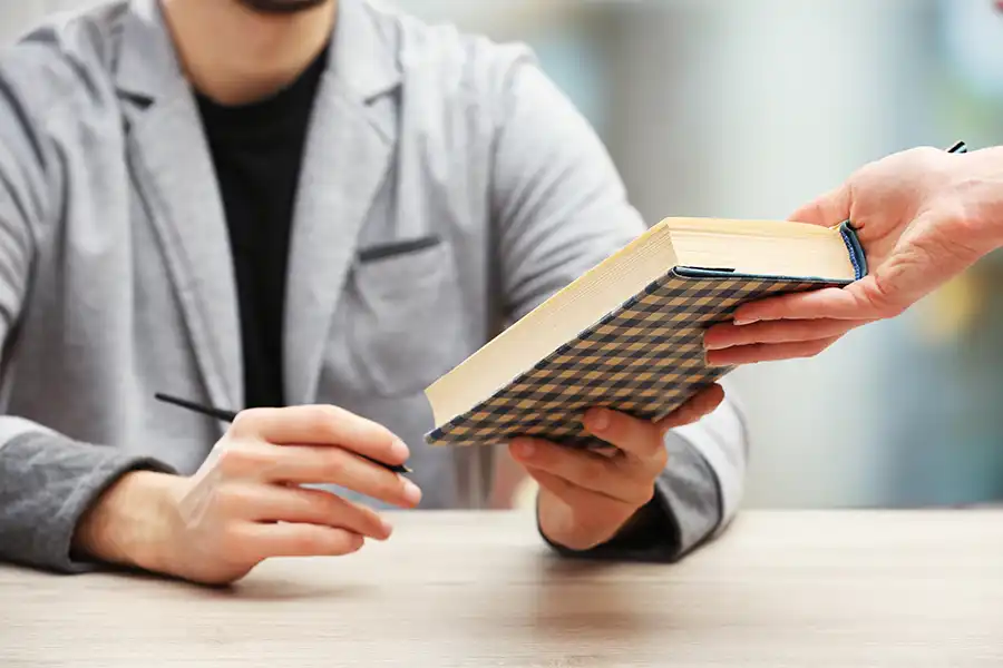 Author signing an autograph in a plaid covered book during a book signing event